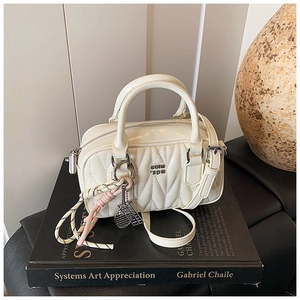 Close-up of quilted cream pillow bag with metal logo and tennis racket charm detail