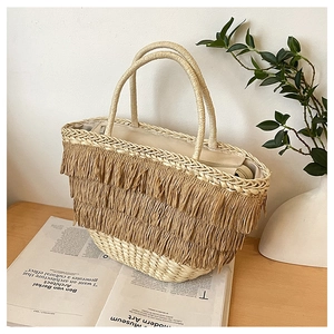 Détail d'un sac à main en paille tressée avec franges et anses rondes sur table en bois