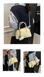 Close-up of cream yellow glossy handbag with silver heart charm and leather straps