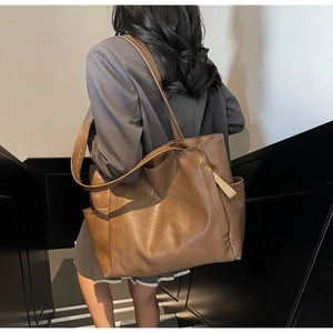 Detail shot of a large brown vintage tote bag showing its rich leather texture and side pocket