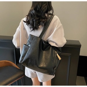 Detail view of large black minimalist tote bag with side pocket and shoulder strap on model