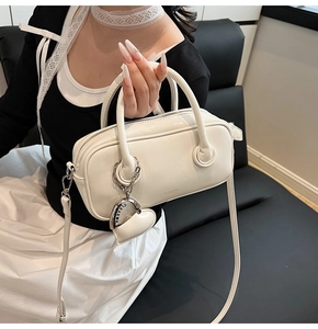 Détail du sac polochon blanc en cuir avec doubles poignées et breloque en cœur