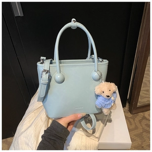 Detail of light blue bucket bag with leather texture and cute teddy bear charm