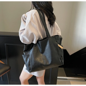 Detail of black pebbled leather tote bag showing side pocket and soft texture with charm
