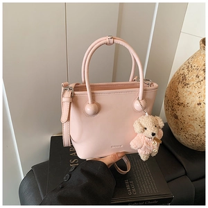 Detail view of pink bucket bag with smooth PU leather, dual handles, and bear charm accessory