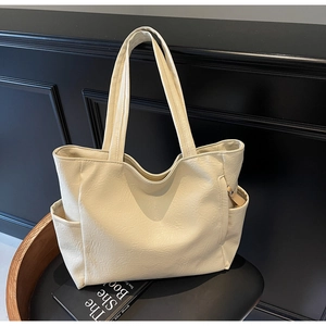 Detail of cream leather tote bag featuring natural grain texture and side pocket design