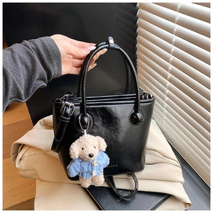 Detail of a black glossy bucket bag featuring a cute plush dog charm in a blue sweater