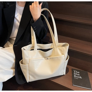 Minimalist cream tote bag with large capacity and soft leather texture on a city model