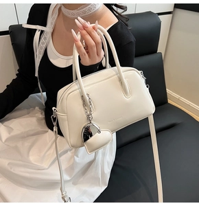 Detail view of cream white boston bag with Rico & Luxury logo and silver heart charm