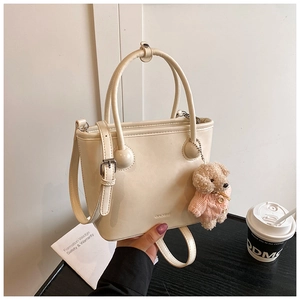 Close-up of a cream bucket bag with brand logo and cute plush bear charm on the handle