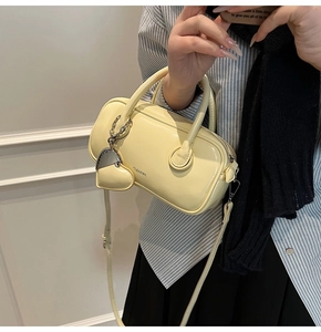 Détail d'un mini sac Boston jaune crème avec pendentif en cœur et bandoulière réglable