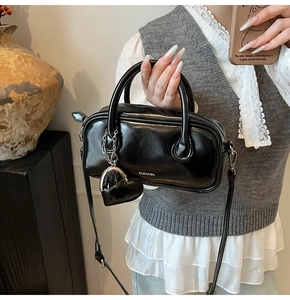 Détail du sac polochon en cuir brillant noir avec logo CLEAR K et pendentif coeur