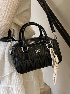 Quilted black Boston bag with pleated texture and silver branding worn with white dress