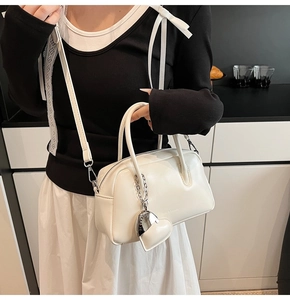 Detailed close-up of a white leather boston bag with a heart charm and metal chain