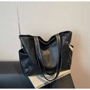 Detail view of black faux leather tote bag with side pockets on a stylish chair