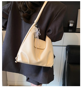 Close-up of off-white lychee leather tote bag with pearl and lace bow charms on model