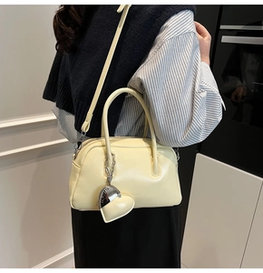 Close-up of cream pillow bag with fine strap and heart pendant detail