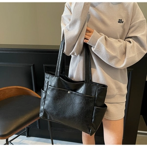 Detail of black faux leather tote bag showing textured surface and metal snap front pocket