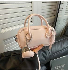 Détail du sac bowling rose clair avec breloque cœur et logo métallique sur cuir lisse