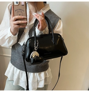 Close-up detail of black glossy handbag with heart charm and thin shoulder strap
