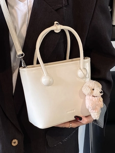 Minimalist beige bucket bag with unique round handle and plush puppy charm detail