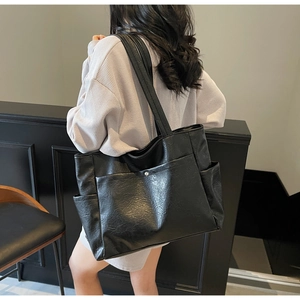 Detail view of black soft leather tote bag with side pockets on a white shirt model