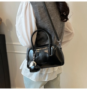 Detail showing glossy black leather bowling bag with heart charm and metallic label