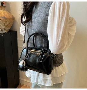 Detail of glossy black leather tote bag with heart pendant and adjustable strap in use