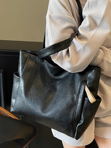 Minimalist black soft leather tote bag with side pocket shown on shoulder in daily life