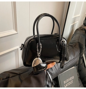 Detail of glossy black pillow bag featuring silver heart pendant and luxury text handle