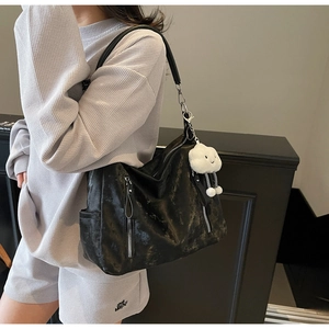 Détail d'un sac cabas noir texturé avec doubles zips et un pendentif nuage en peluche blanc