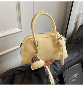 Detail of a creamy yellow patent leather Boston bag with a heart-shaped metal pendant
