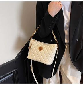 Detail of cream quilted bucket bag with golden round clasp and chain handle