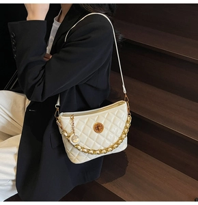 Detail of cream quilted bucket bag featuring a gold turn-lock and elegant chain strap