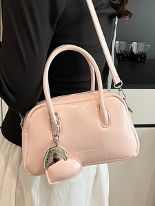 Minimalist light pink glossy handbag with heart charm shown on model in a casual setting