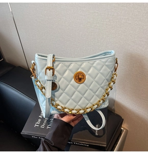 Detail of light blue quilted bucket bag featuring a gold disc lock and chunky metal chain