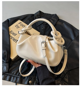 Close-up of cream pleated cloud bag featuring knotted handle and embossed logo detail
