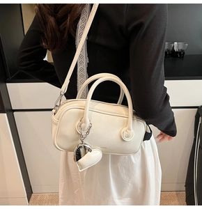Detail showing the cream pillow bag with adjustable strap and heart charm on a model