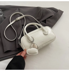Detail view of white cylinder leather bag with CLEAR K logo and heart-shaped charm accessory