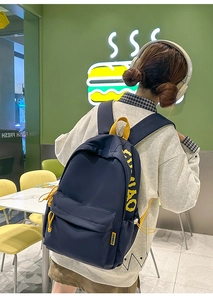Detail showing contrast navy nylon backpack with yellow zipper pulls and brand label