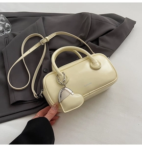 Detail of a creamy white Boston bag with heart charm on a gray blazer backdrop