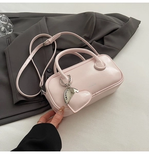 Detail of light pink Boston handbag featuring a heart charm on a grey blazer