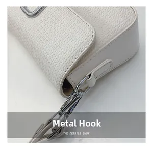Close-up of bright silver metal hook and woven texture on a white crossbody bag