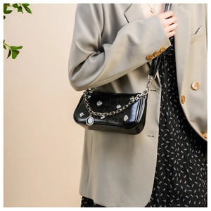 Detail of black patent leather underarm bag with silver chain and heart charms on model