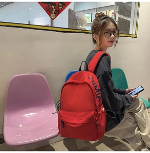 Detail of red water-resistant nylon backpack showing large side logo and zipper pocket