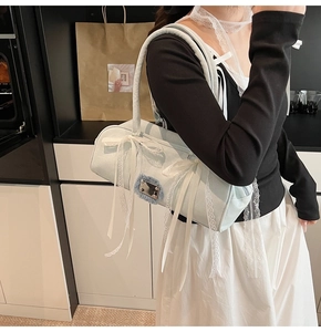 Detail der hellblauen Denim-Schultertasche mit weißen Spitzenschleifen und Silberplakette