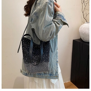 Detail of a black bucket bag with white crystal studs worn by a model in denim jacket