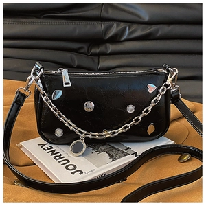 Detail of black glossy leather bag with silver studs and chain on a magazine