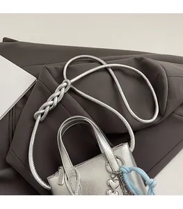 Detail of silver bucket bag featuring woven shoulder strap and heart-shaped metal pendant