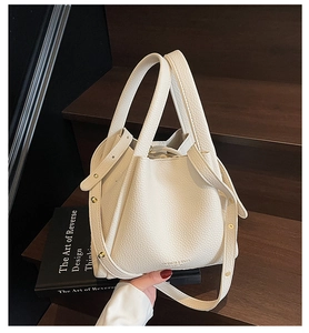 Detailed macro view of the off-white lychee pattern leather bucket bag and gold rivet strap